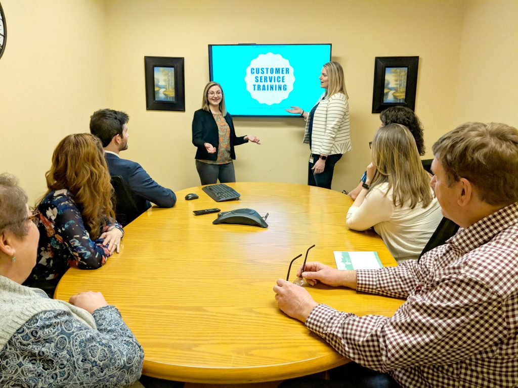 Leslie Mattison and Laura Kay give a presentation during a customer service training in the conference room as our team listens