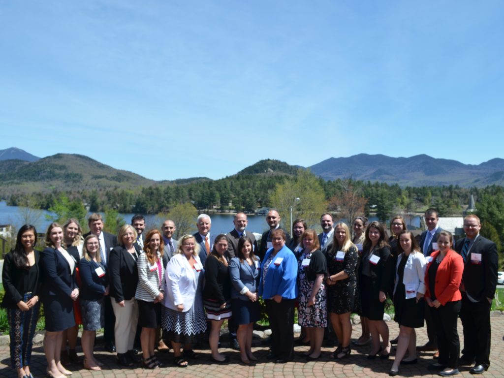 Our Atria 340B team standing in front of mirror lake and the mountains in Lake placid NY
